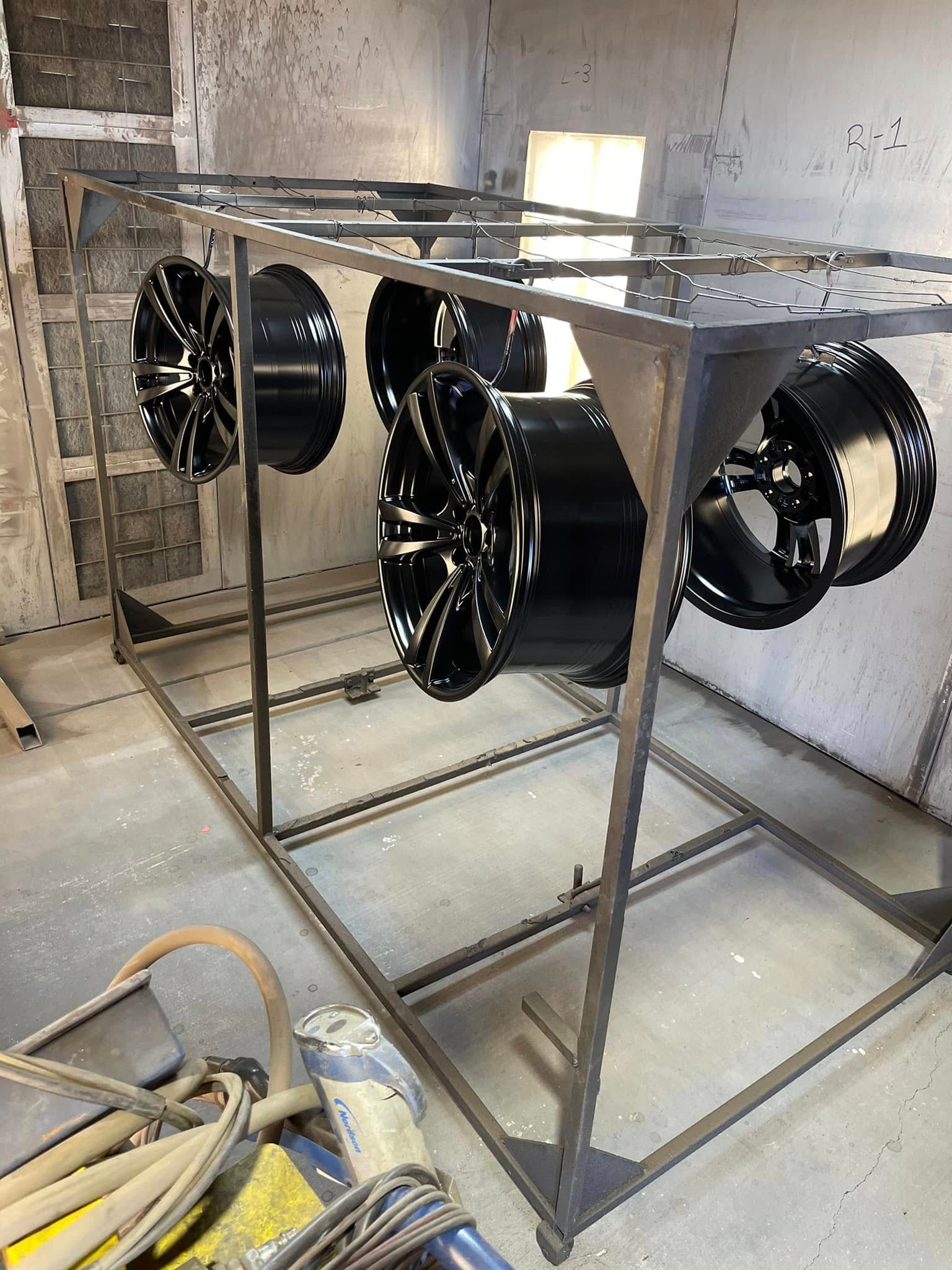 Black powder coated alloy wheels hanging on a rack in the spray booth